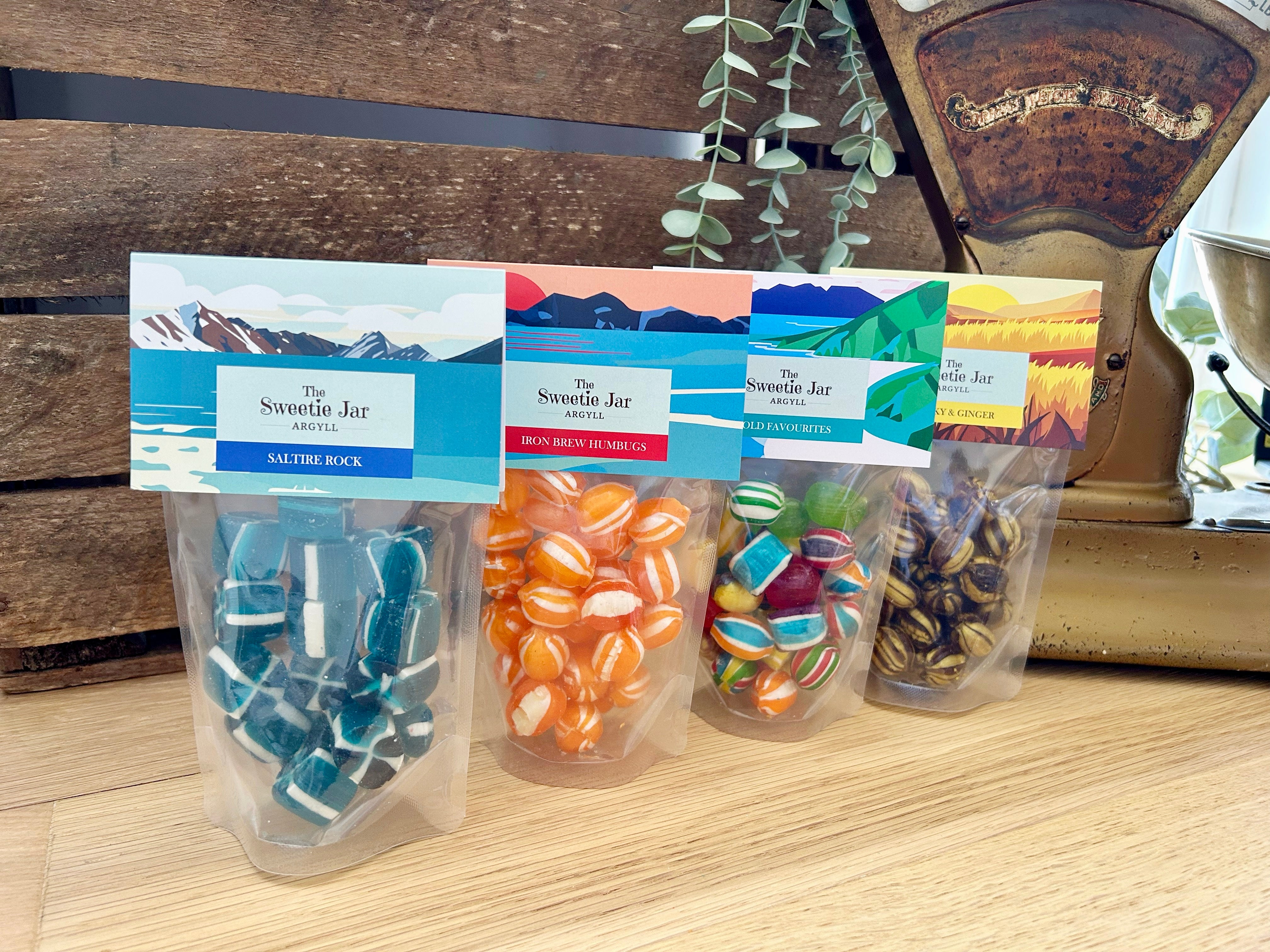 Four packages of 'The Sweetie Jar' sweets on a wooden surface with a decorative background.