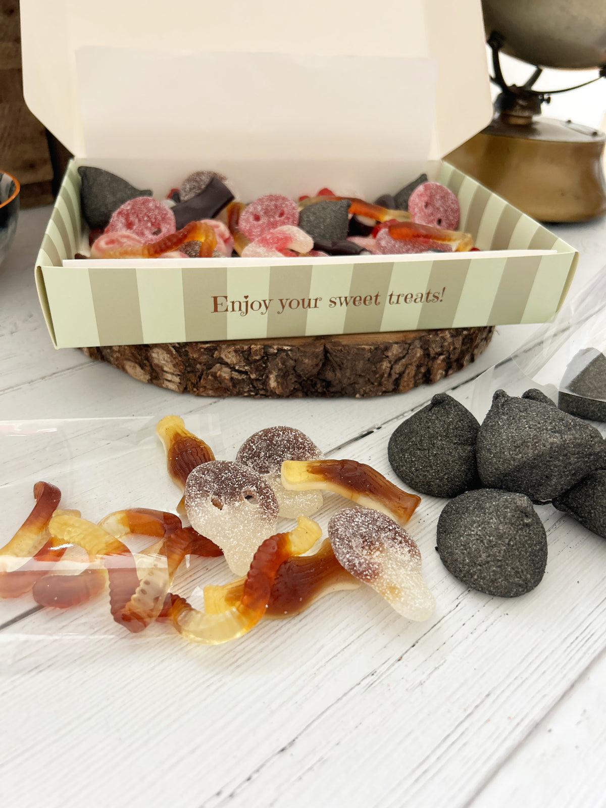 Varied Halloween pick 'n' mix sweets in a striped sweetie box sitting on white wooden surface.