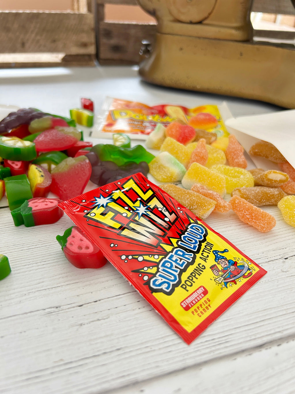 Summery Pick 'n' Mix sweets spilling out of white pouch packaging, double dip and fizz wiz sweets on white wooden surface.