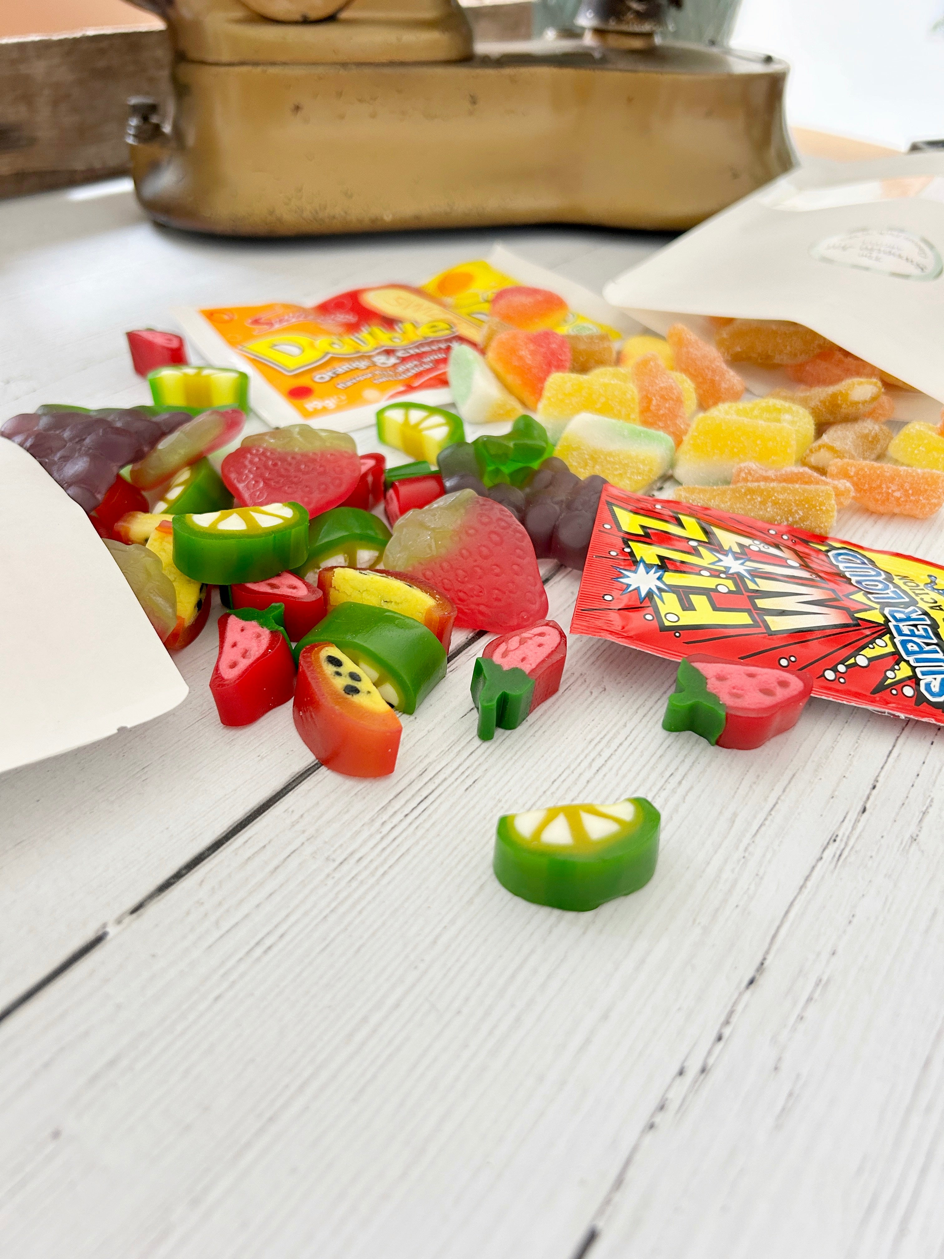 Summery Pick 'n' Mix sweets spilling out of white pouch packaging, double dip and fizz wiz sweets on white wooden surface.