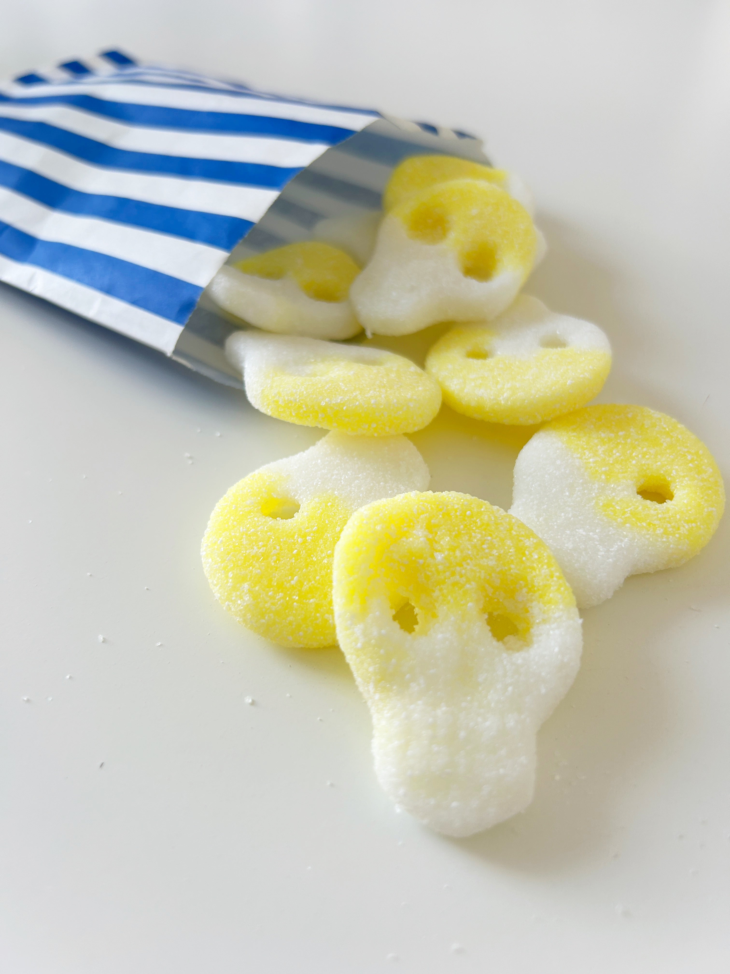 Sugar skull-shaped candies spilling out of a blue and white striped paper bag on a white surface.