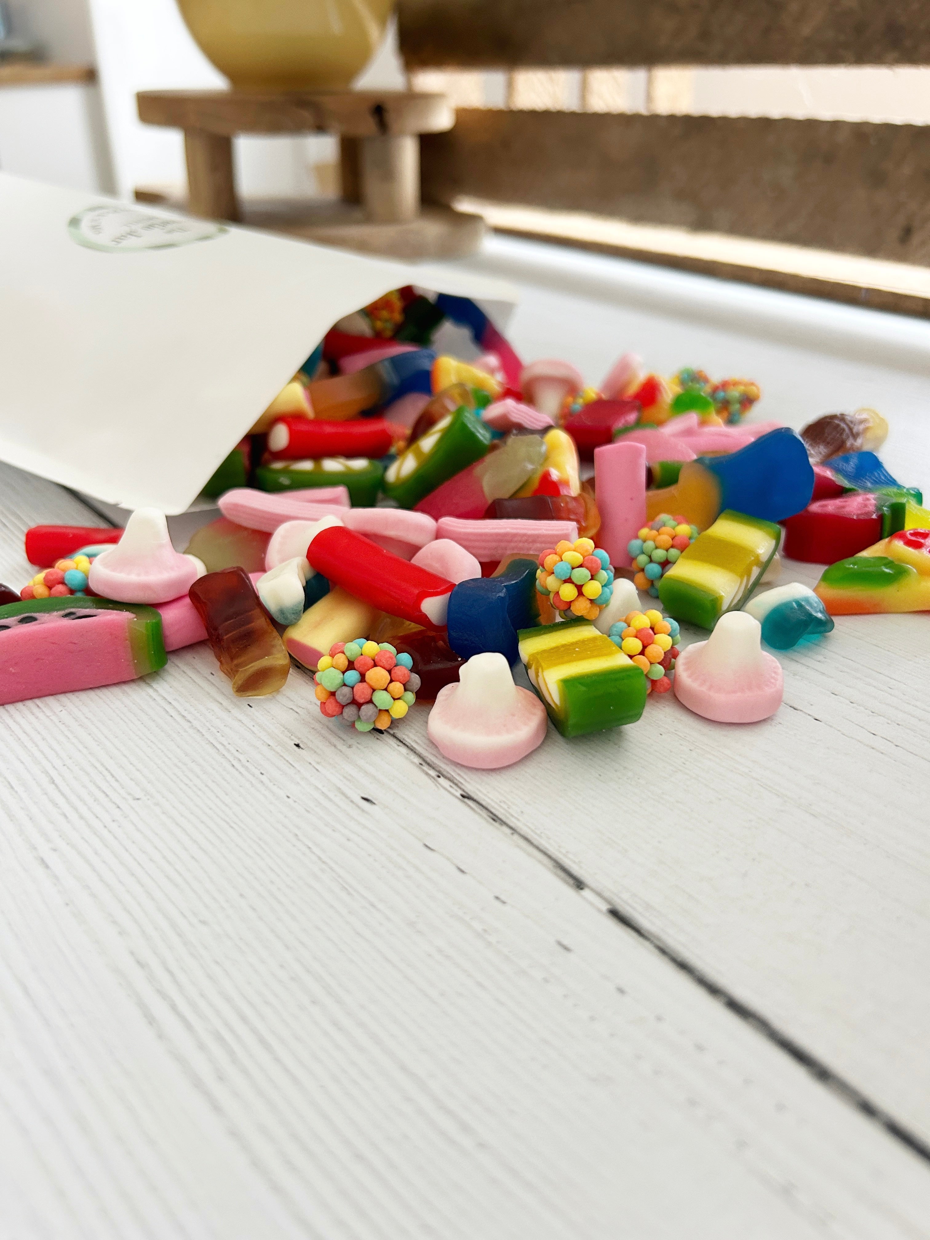The Sweetie Jar custom pick 'n' mix pouch with sweets spilling out of it onto white wooden surface.