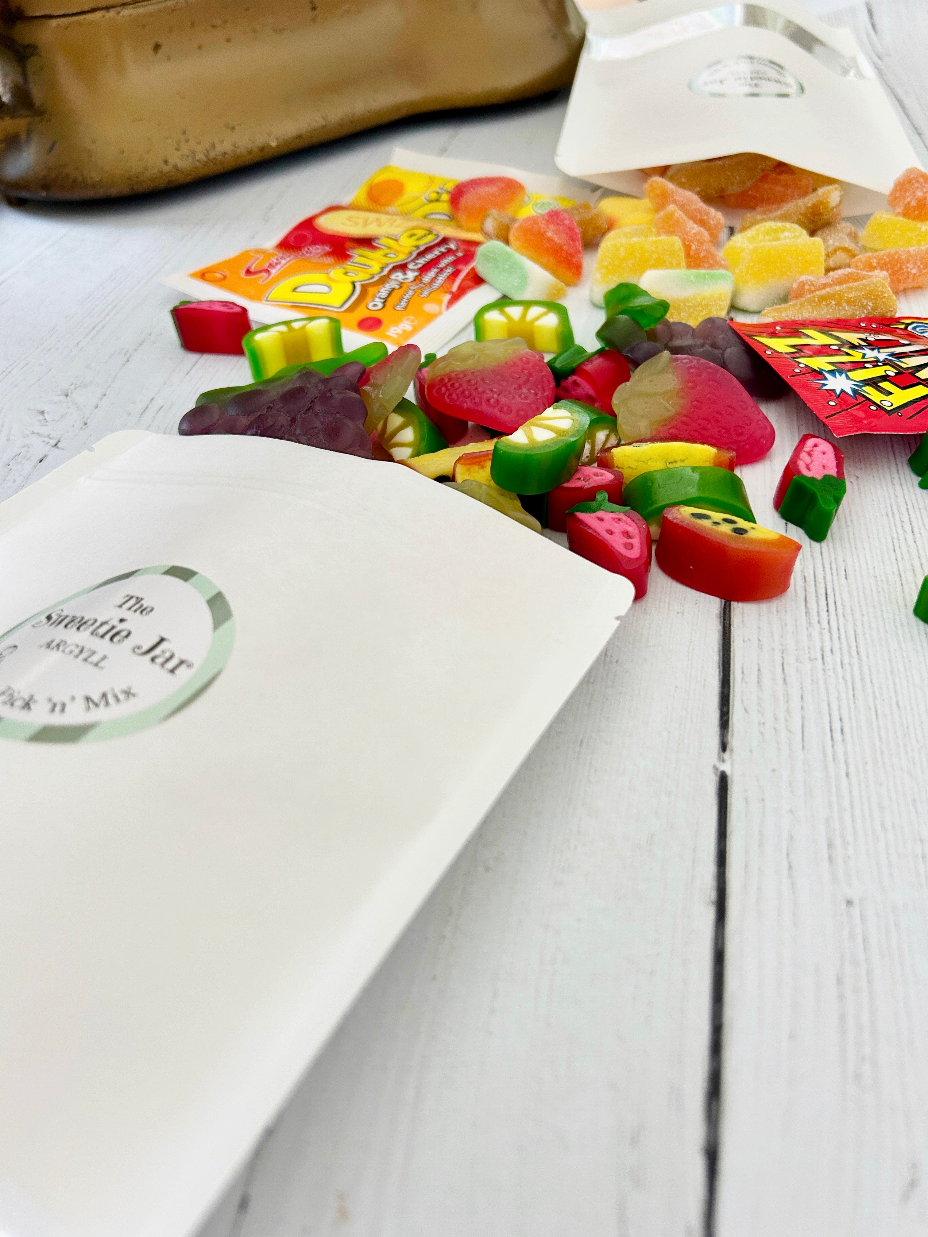 Summery Pick 'n' Mix sweets spilling out of white pouch packaging, double dip and fizz wiz sweets on white wooden surface.