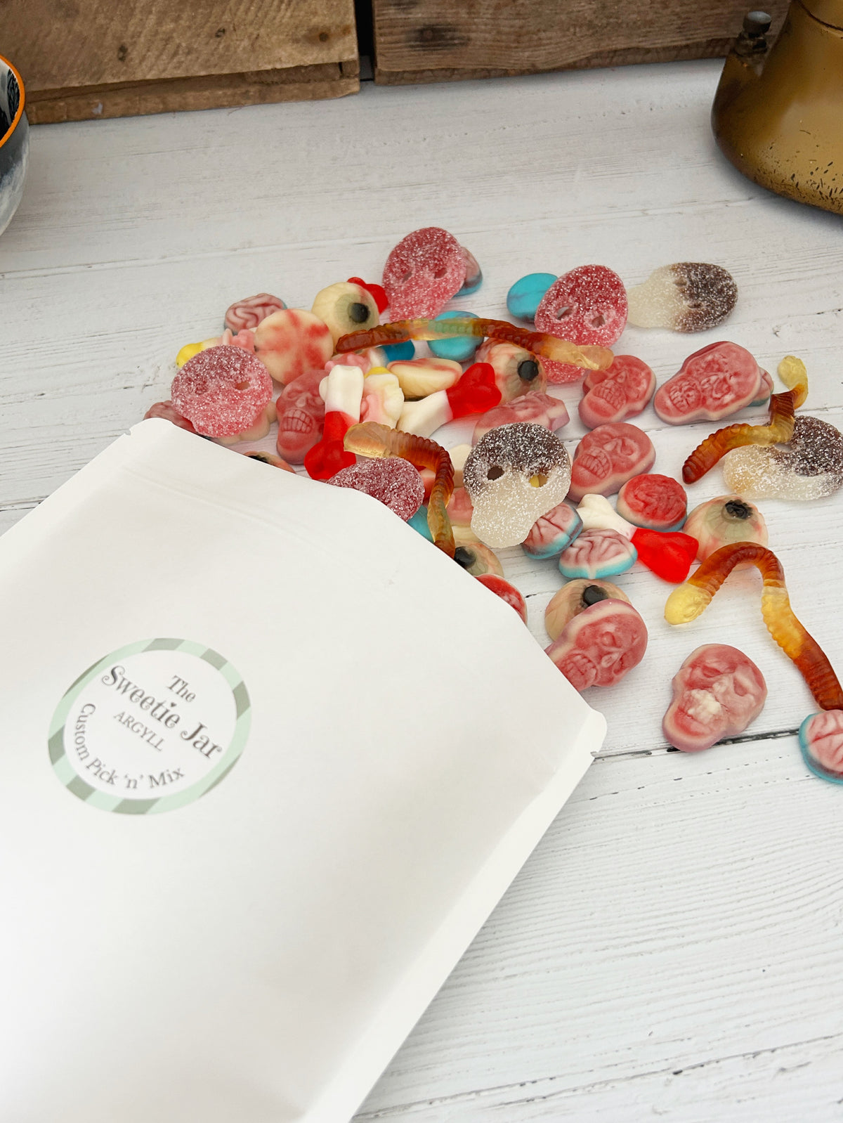 A close-up of assorted pick 'n' mix sweets spilled onto a white wooden surface, including brain-shaped gummies, worm gummies, and eye gummies.