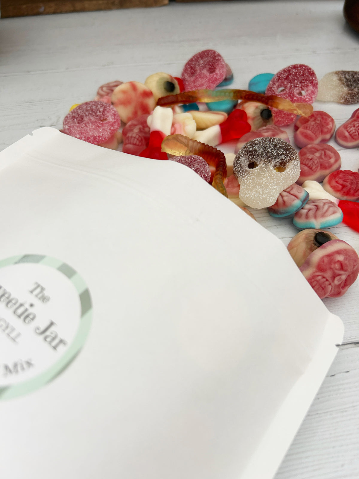 A close-up of assorted pick 'n' mix sweets spilled onto a white wooden surface, including brain-shaped gummies, worm gummies, and eye gummies.
