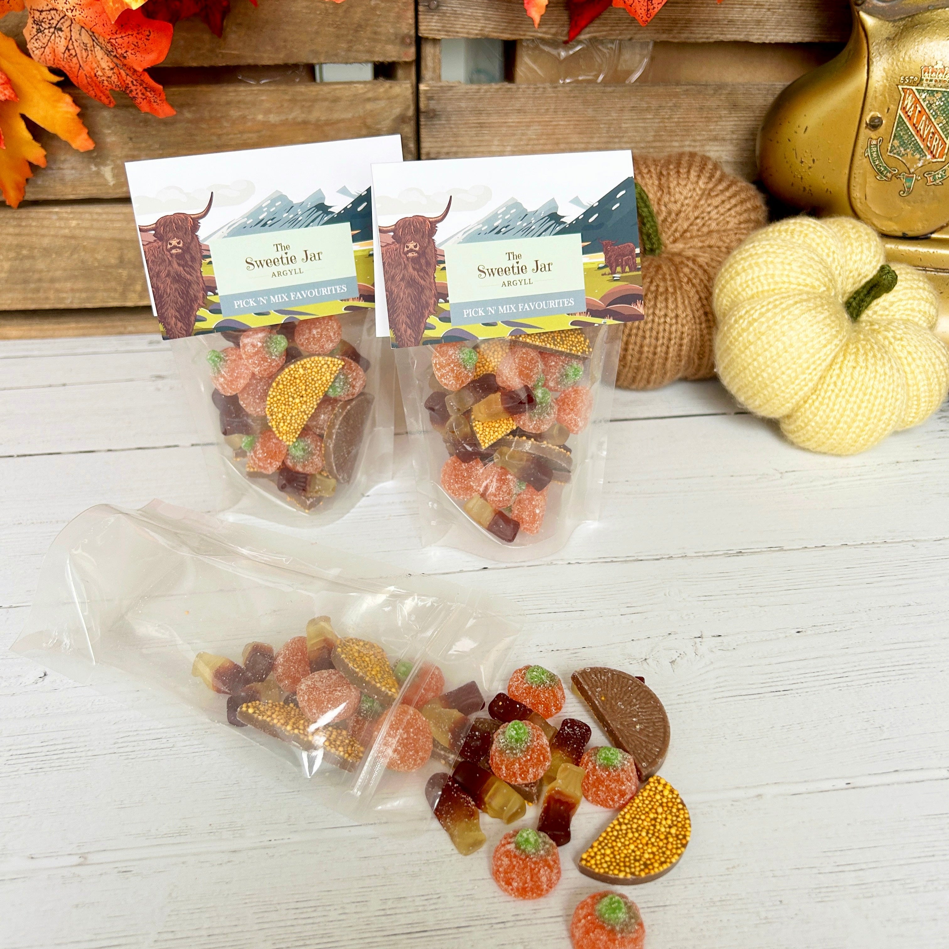 Packets of autumn-themed gummy candies on a wooden surface with decorative leaves and pumpkins.