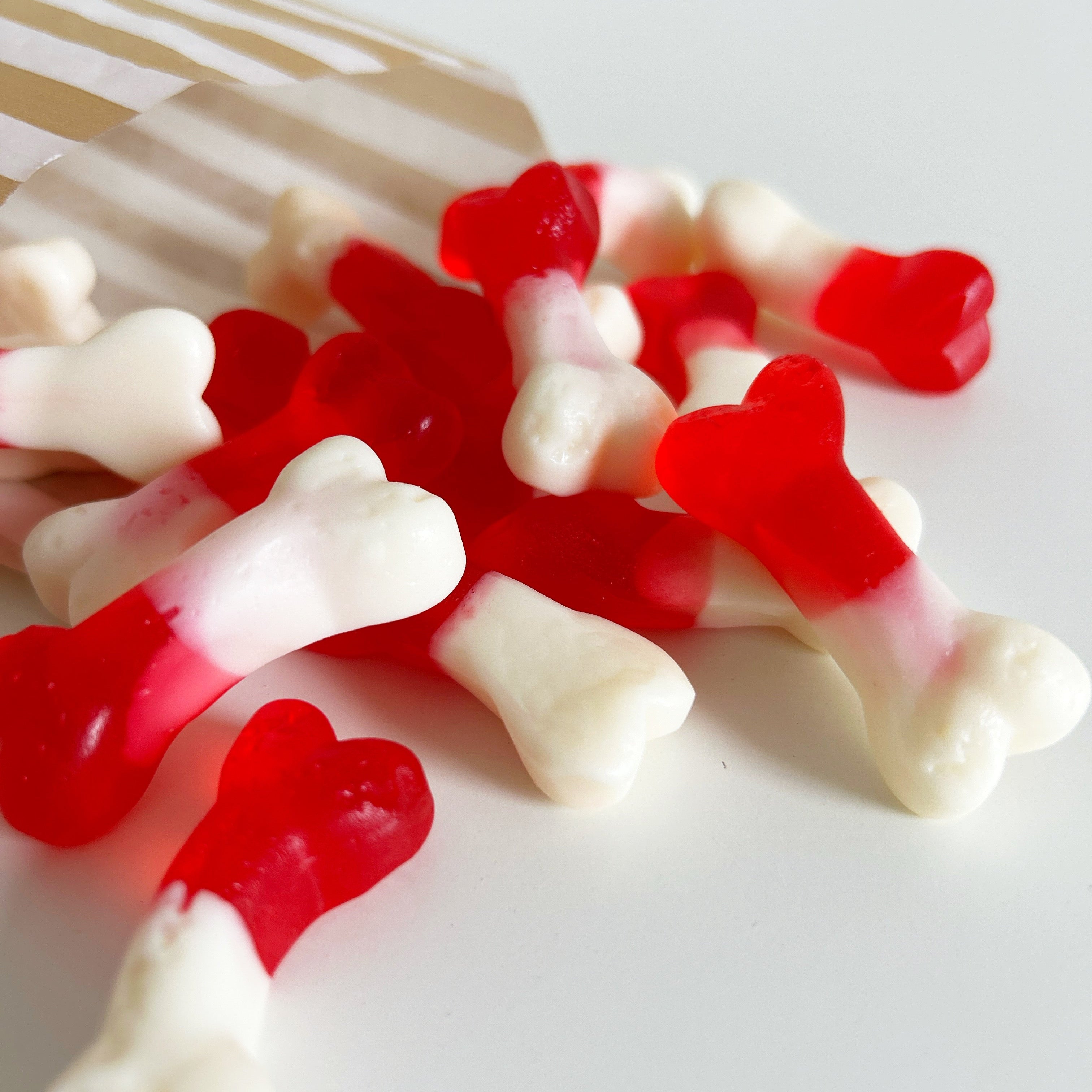 Red and white gummy candy shaped like bones on a white background