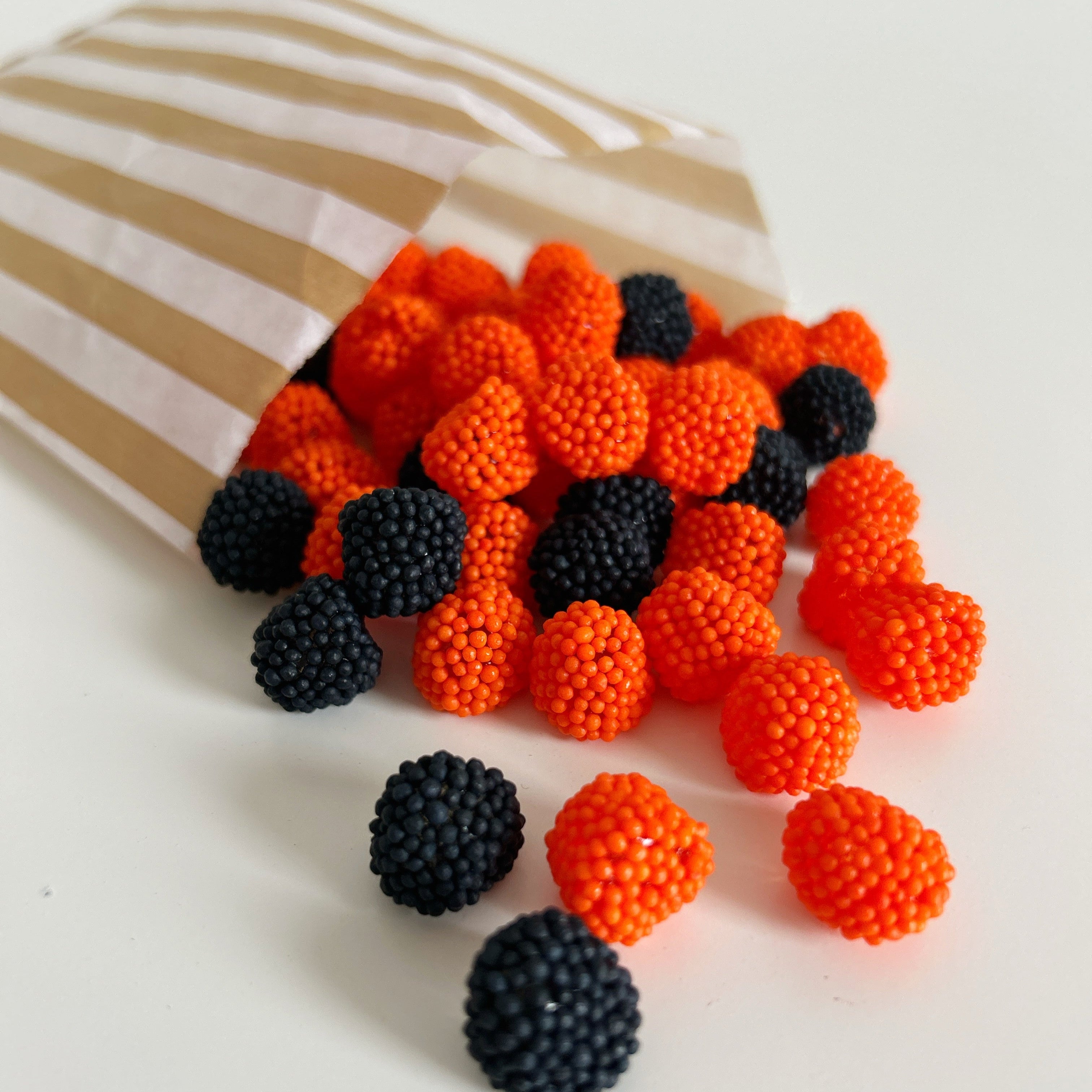 Orange and black spherical candies spilling out of a striped paper bag on a white background