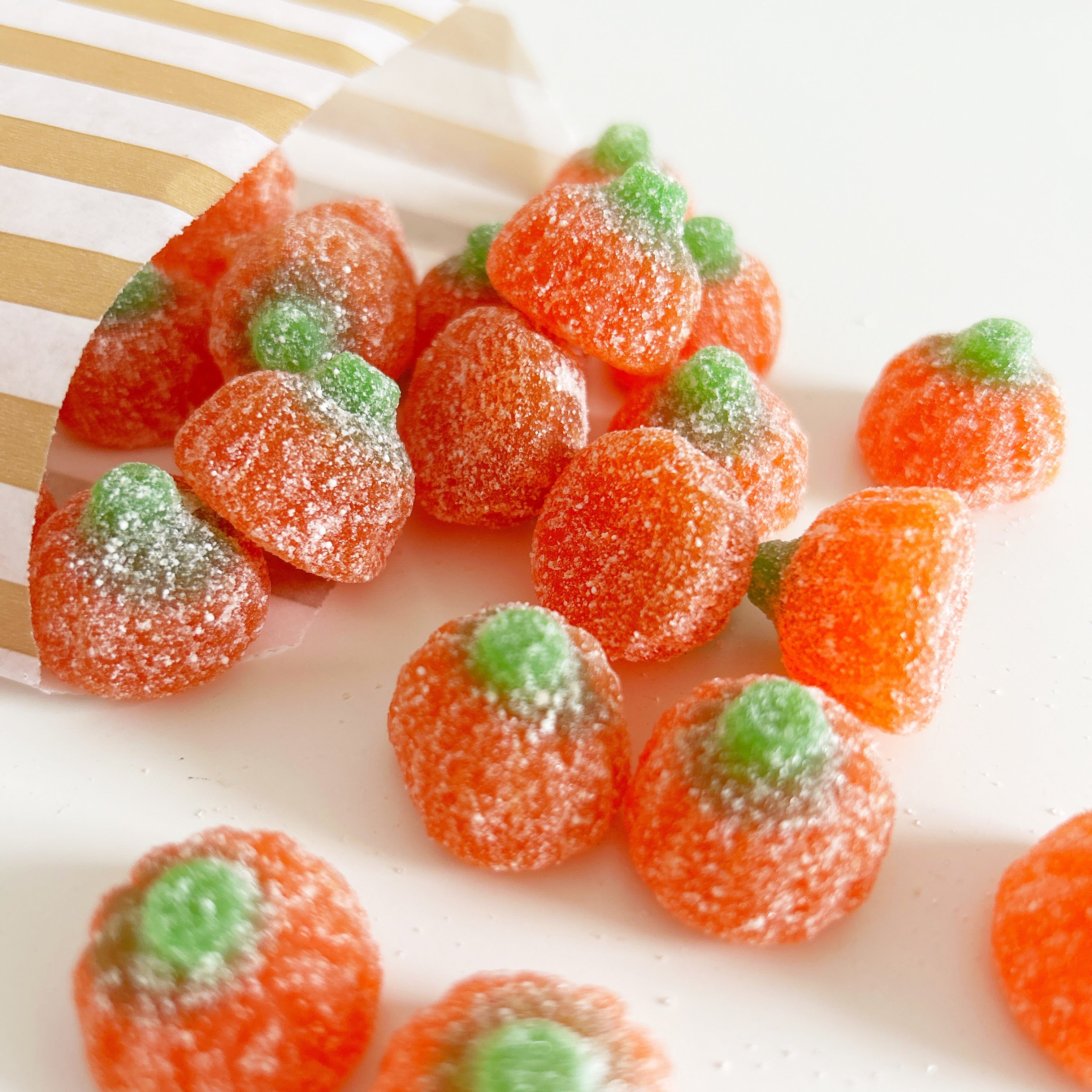 Gummy candy shaped like pumpkins with green stems on a white surface.