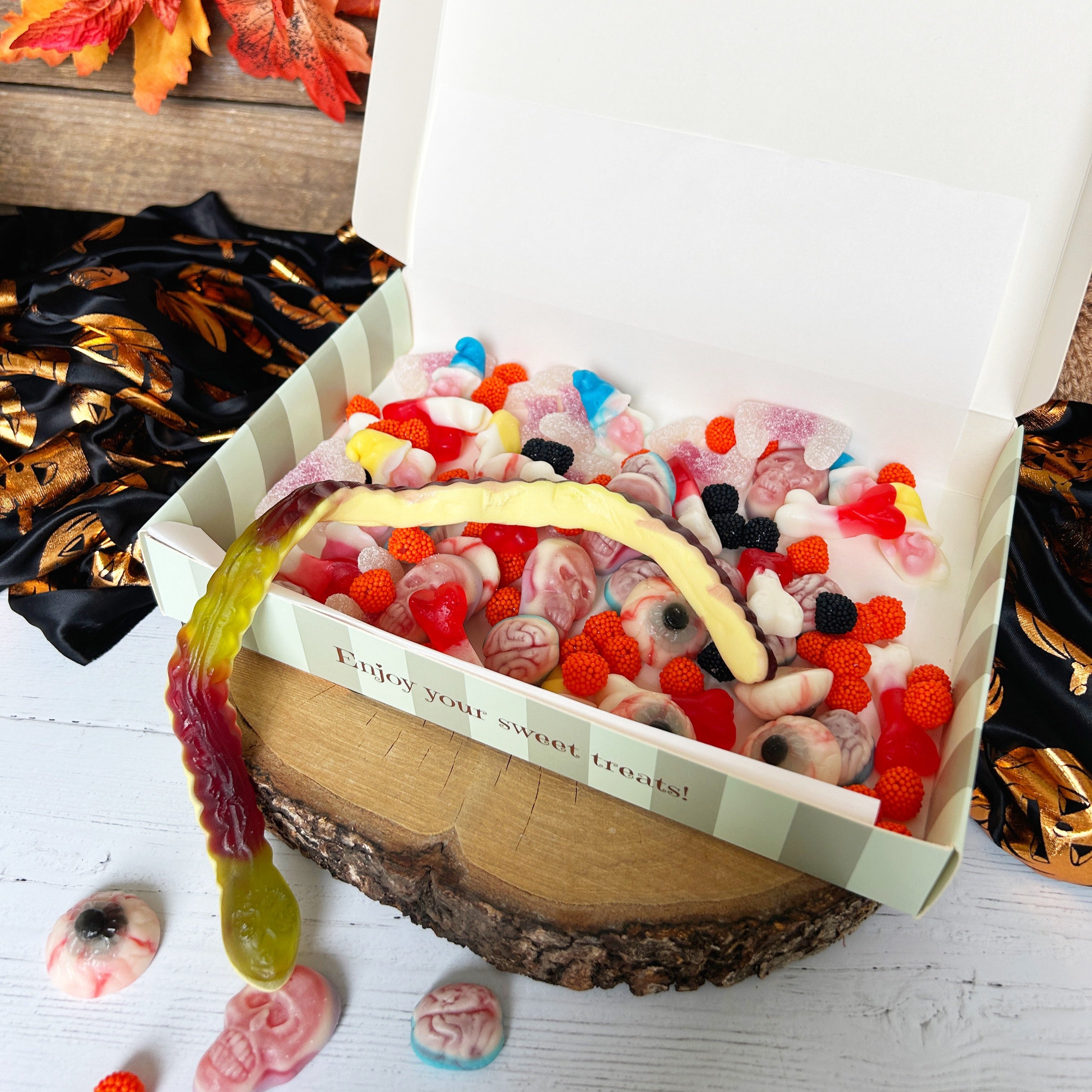 Box of assorted gummy candies with a decorative label on a wooden surface with autumn leaves.