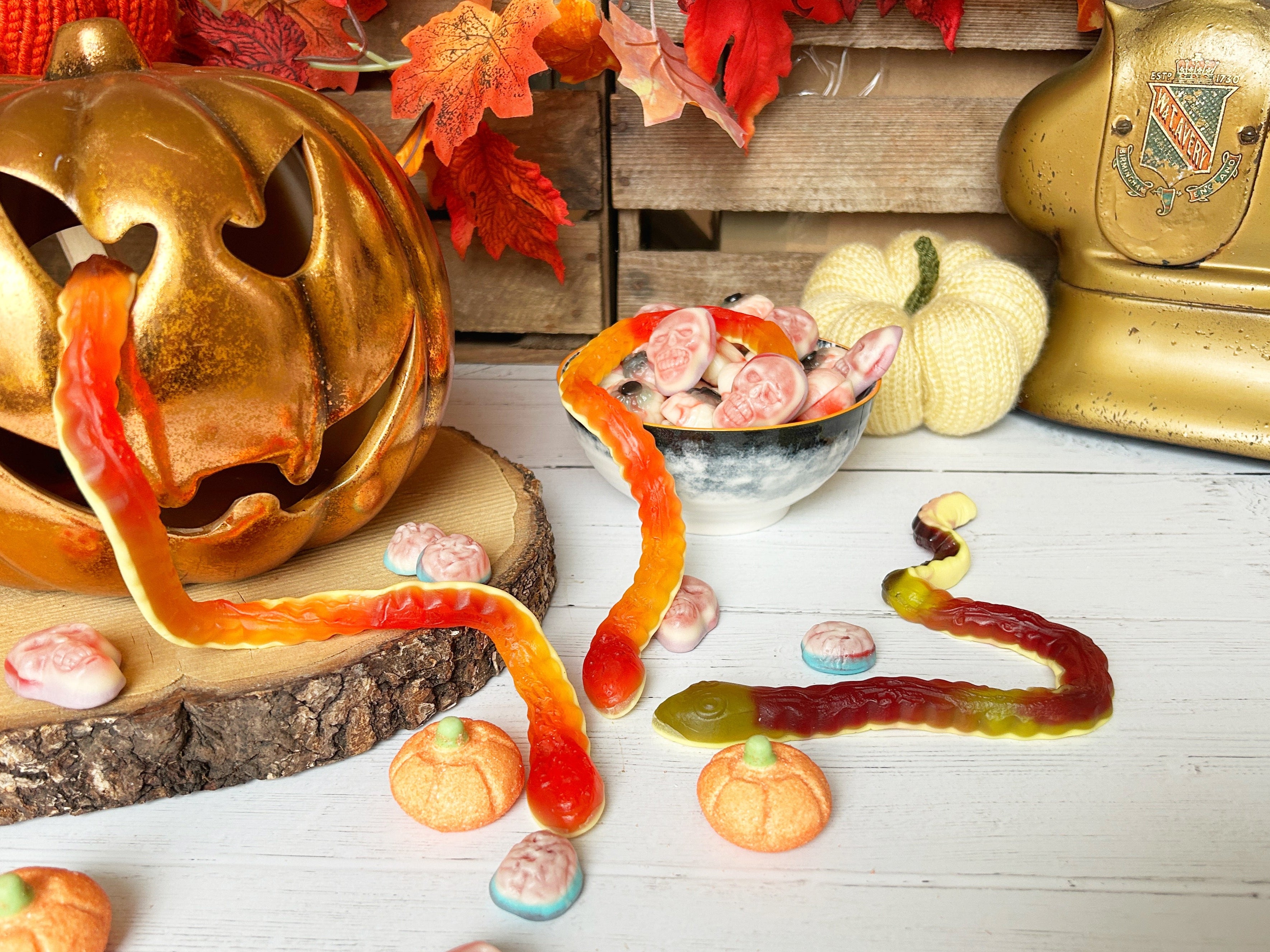 Halloween-themed display with gummy worms, candy, and decorative pumpkins on a wooden surface.